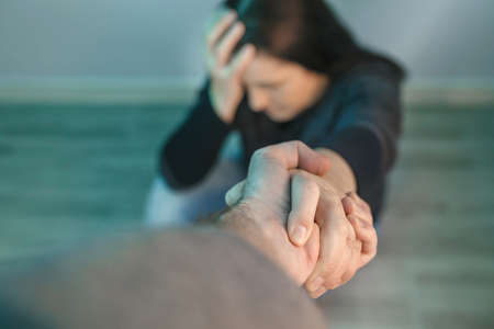 Unrecognizable woman with mental health problems receiving help from man holding her hand. Helping hand conceptの写真素材