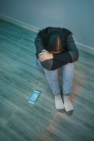 Top view of unrecognizable desperate woman with phone addiction covering her face with mobile on the...
