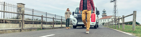 Man with jerrycan walking along the road looking for help for his broken down camper van while his wife calls on the phoneの写真素材