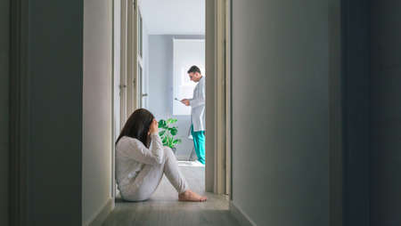 Female patient in pajamas sitting on the floor in the corridor of a mental health center with a...