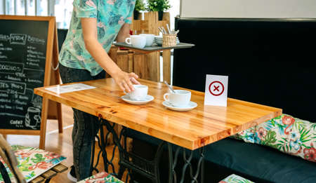Waitress picking up cups from a table that has a no use signの写真素材