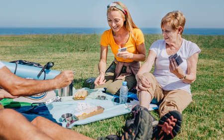 Young woman and senior woman playing cards in family during an excursion sitting on a blanket outdoorsの写真素材