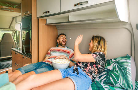 Young woman throwing a popcorn into her boyfriends mouth having fun lying on the bed of their camper...