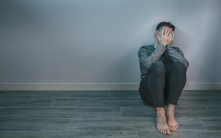 Unrecognizable man with problems crying while covering his face with hands sitting on the floor