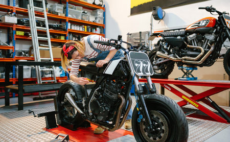 Mechanic woman with screwdriver repairing custom motorcycle over platform on factoryの写真素材