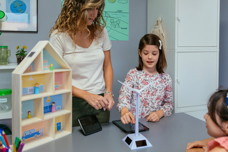 Female student next to teacher showing solar windmill to classmate in ecology classroom. Renewable...
