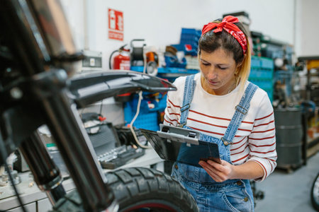 Concentrated female mechanic with clipboard reviewing information of motorcycle on garageの写真素材