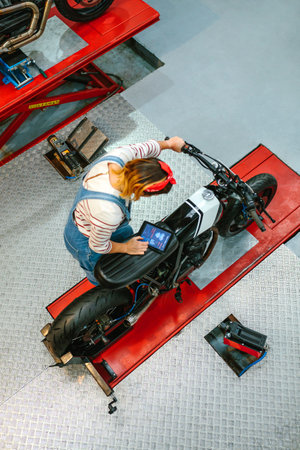 Top view of mechanic woman using a diagnosis app in digital tablet to review custom motorcycle on factoryの写真素材