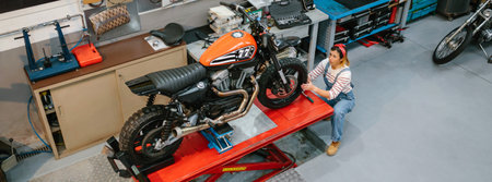 Top view of mechanic woman reviewing custom motorcycle over platform on factoryの写真素材
