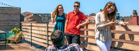 Group of happy friends talking in rooftop city while woman looking her phone on a sunny day