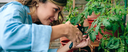 Portrait of young woman gardener using pruning shear to trim plant leaves of urban garden on terrace of residential apartmentの写真素材