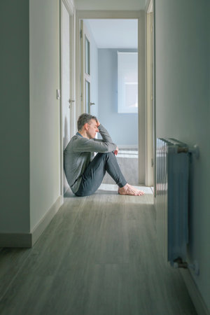 Desperate man with mental disorder and suicidal thoughts holding his head with hand sitting on the floor of a mental health centerの写真素材