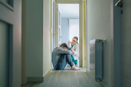 Female doctor trying to help male patient with mental disorder who refuses help sitting on the floor...