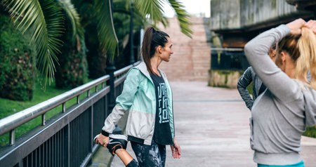Happy brunette woman runner stretching leg next to her female friends before training on townの写真素材