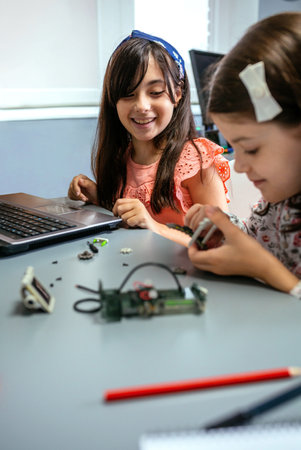 Portrait of happy female student smiling while looking to classmate assembling machine pieces in a robotics class. Elementary technological education concept.の写真素材