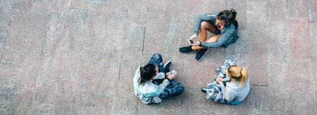 Top view of happy women friends runners relaxing and talking sitting on the floor after urban trainingの写真素材