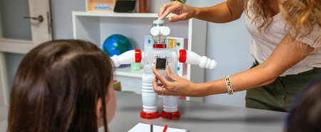 Unrecognizable female teacher in a robotics class explaining to her students how to connect solar panel on recycled toy robot made with plastic packages. Sustainable technological education concept.の写真素材