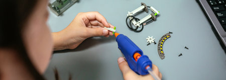 Close up of unrecognizable female young student using hot melt glue gun on machine pieces in a robotics class. Elementary technological education concept.の写真素材