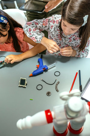 Concentrated female student assembling machine pieces next to her teacher and to other schoolchild...