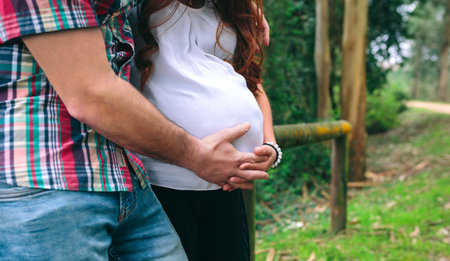 Unrecognizable latin female pregnant and her partner holding belly on nature