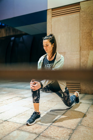 Concentrated young brunette woman runner with ponytail stretching her legs behind of banister before...