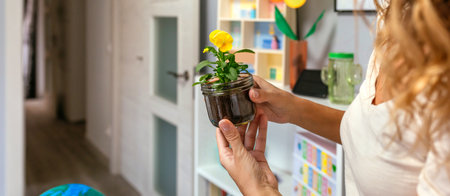 Unrecognizable curly blonde woman holding a pansy plant inside of glass pot in ecology classroom....