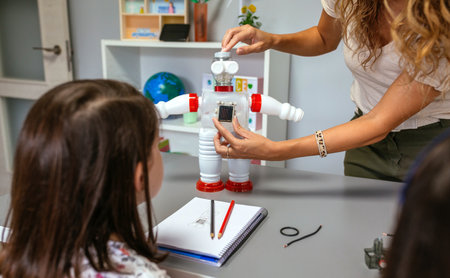 Unrecognizable female teacher in a robotics class explaining to her students how to connect solar panel on recycled toy robot made with plastic packages. Sustainable technological education concept.の写真素材