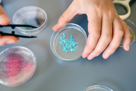 Close up of female scientist hand holding a blue glitter sample over petri dish on a environment...