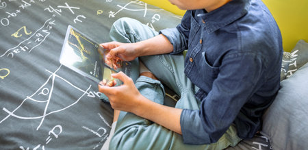 Unrecognizable young kid holding digital display with glass screen while watching videos sitting...