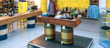 Banner of empty clothing store with industrial style decoration. Interior of retro local wear shop with clothes over wooden counter supported by fuel barrels. Small business concept. No People.の写真素材