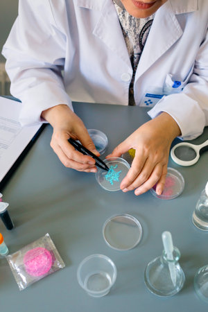 Unrecognizable female scientist analyzing a blue glitter sample over petri dish on a environment...