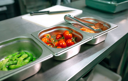 Close up of metal containers with cherry tomatoes, salmon and green beans are arranged on stainless steel table, ready for cooking, in empty restaurant kitchenの写真素材