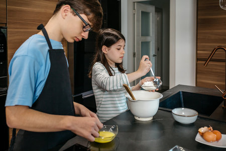 Boy and young girl preparing together homemade cake, pouring ingredients in bowl and sharing...