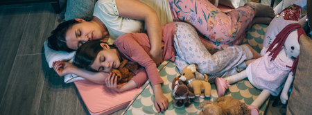 Banner of mother embracing to little daughter with closed eyes asleep surrounded by cushions at night. Loving woman and girl sleeping together lying over mats. Security and family protection concept.の写真素材