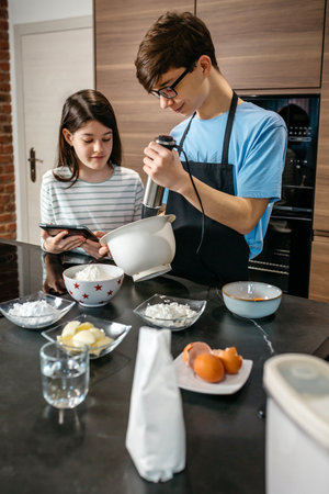 Smiling teenage brother showing mixed ingredients for a cake inside of bowl to happy and curious...
