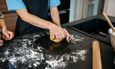 Close up of unrecognizable teenage boy with apron kneading dough while receives guidance from his...