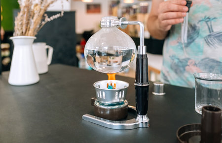 Close up of Japanese coffee maker boiling water while unrecognizable barista wait to put siphon and make a fresh specialty coffee. Traditional brewing method highlight the art of coffee preparation.の写真素材