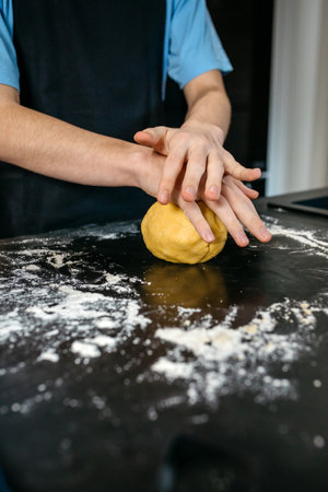 Close up of chef hands kneading fresh pasta dough on a dark, flour dusted kitchen counter, showcasing the art of culinary creation in a modern kitchen setting. Copy space available in image lower areaの写真素材