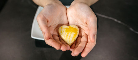 Banner of unrecognizable female pastry chef hands holding a freshly baked heart shaped cookie with egg glaze, showcasing her passion and love for bakingの写真素材