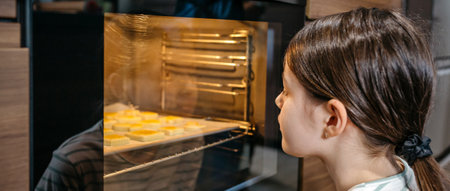 Banner of girl watching cookies baking in oven, waiting for them to be ready, enjoying the smell and anticipating delicious taste. Cooking at leisure time concept. Left copy space available.の写真素材