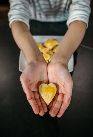 Unrecognizable female pastry chef hands holding a freshly baked heart shaped cookie with egg glaze, showcasing her passion and love for bakingの写真素材