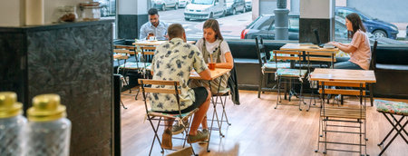 Banner of customers enjoying coffee and working on laptops in a bright, inviting cafe, capturing the essence of modern cafe culture and urban lifestyle in a lively and social atmosphereの写真素材