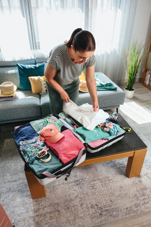 Woman packing clothes into her suitcase with care, preparing for an exciting summer vacation, surrounded by travel accessories and various clothing items, ready for adventureの写真素材