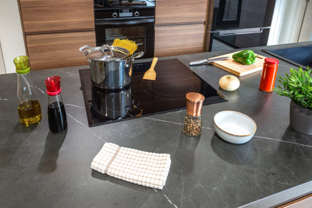 Ingredients for cooking spaghetti arranged on modern kitchen counter. Olive oil, soy sauce, salt, pepper, onion, green pepper, tomato sauce, spaghetti and pot near an induction hob ready for cookingの写真素材