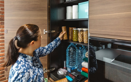Woman preparing emergency food pantry in kitchen for disasters. Alert, foresight and self sufficiency strategy for electrical blackout. Female placing cookies package to 72 hours survival kit stored.の写真素材