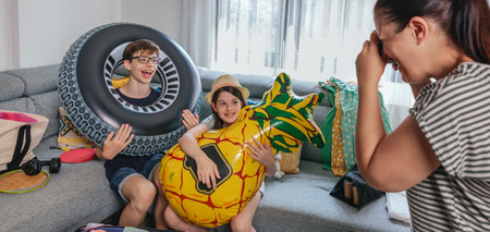 Happy mother taking pictures of her children making funny faces with inflatable pineapple and giant...