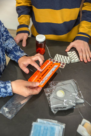 Unrecognizable mother showing how to use medical injection with pre filled syringe to son while organizing first aid emergency kit, providing healthcare guidance and education. 72 hour survival kit.の写真素材