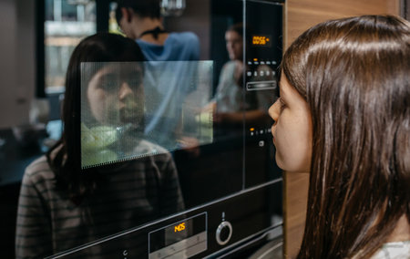 Girl carefully observing butter bowl heating inside modern microwave oven, reflecting her image in the glass door, in a contemporary kitchen settingの写真素材