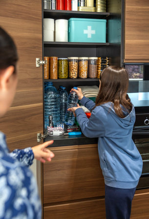 Unrecognizable family organize water bottles in stocked pantry along with canned food and first aid kit, highlighting commitment to government recommendations about emergency or war preparedness.の写真素材