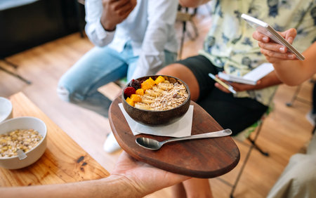 Unrecognizable chef showing vegan breakfast bowl made with mango, banana, raspberries, cereals and muesli to food bloggers and influencers taking pictures with smartphones in cooking master class.の写真素材